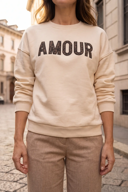 Mujer vistiendo sudadera beige con la palabra AMOUR en letras oscuras y pantalones marrones.