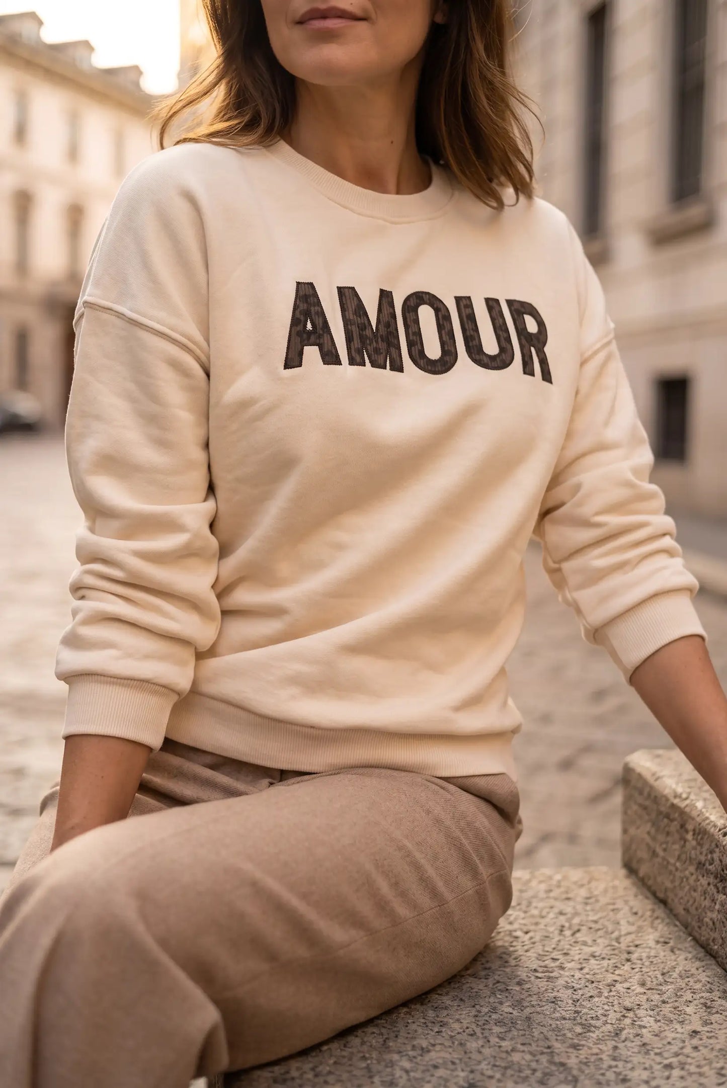 Mujer vistiendo sudadera color crema con el texto AMOUR en el pecho y pantalones beige.