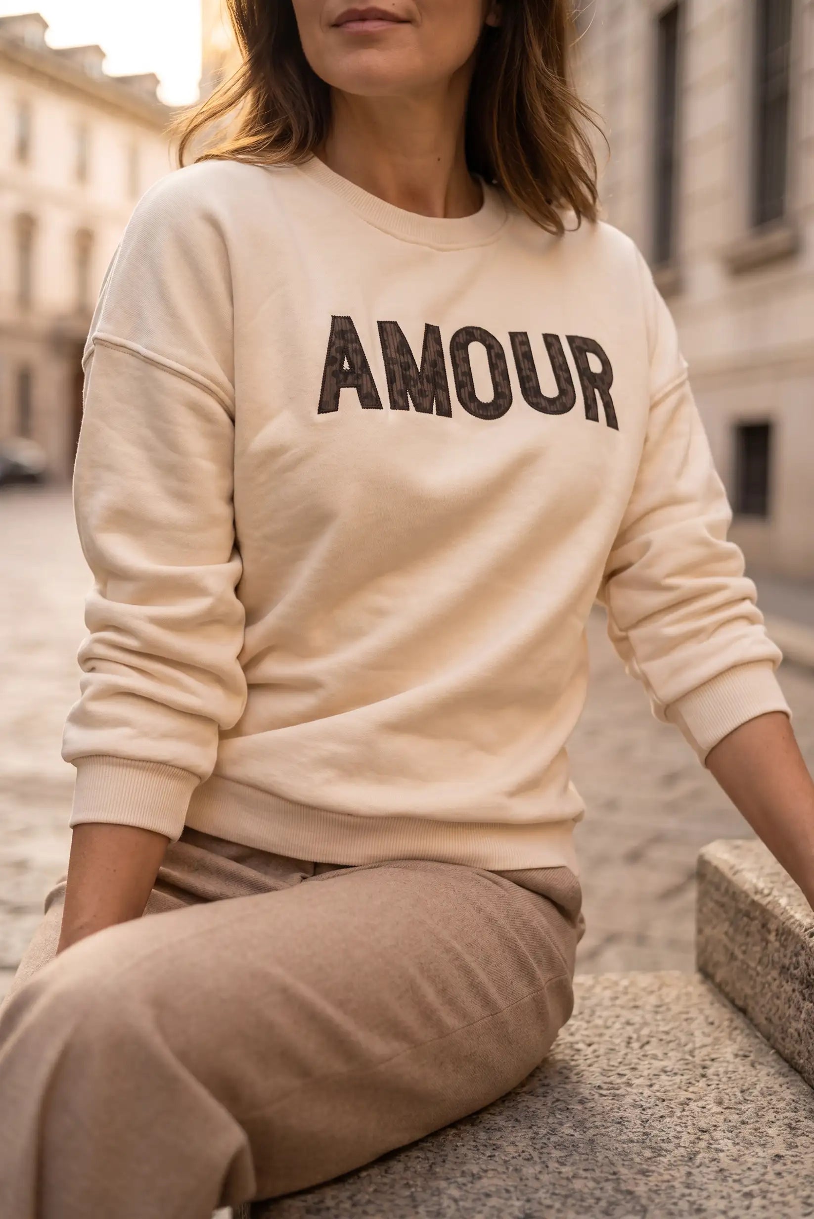 Mujer vistiendo sudadera color crema con el texto AMOUR en el pecho y pantalones beige.
