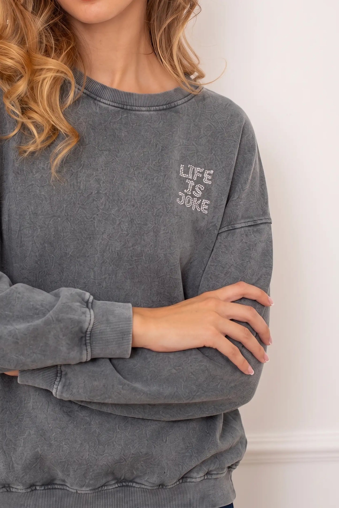 Sudadera gris lavada para mujer con texto brillante 'LIFE IS A JOKE' en el pecho.