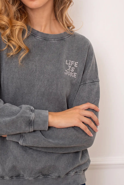 Sudadera gris lavada para mujer con texto brillante 'LIFE IS A JOKE' en el pecho.