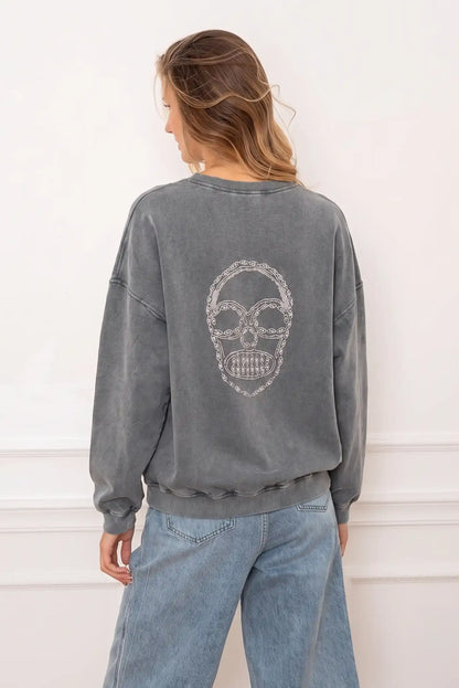 Mujer de espaldas con sudadera oversize gris oscuro con diseño de calavera blanca y vaqueros claros