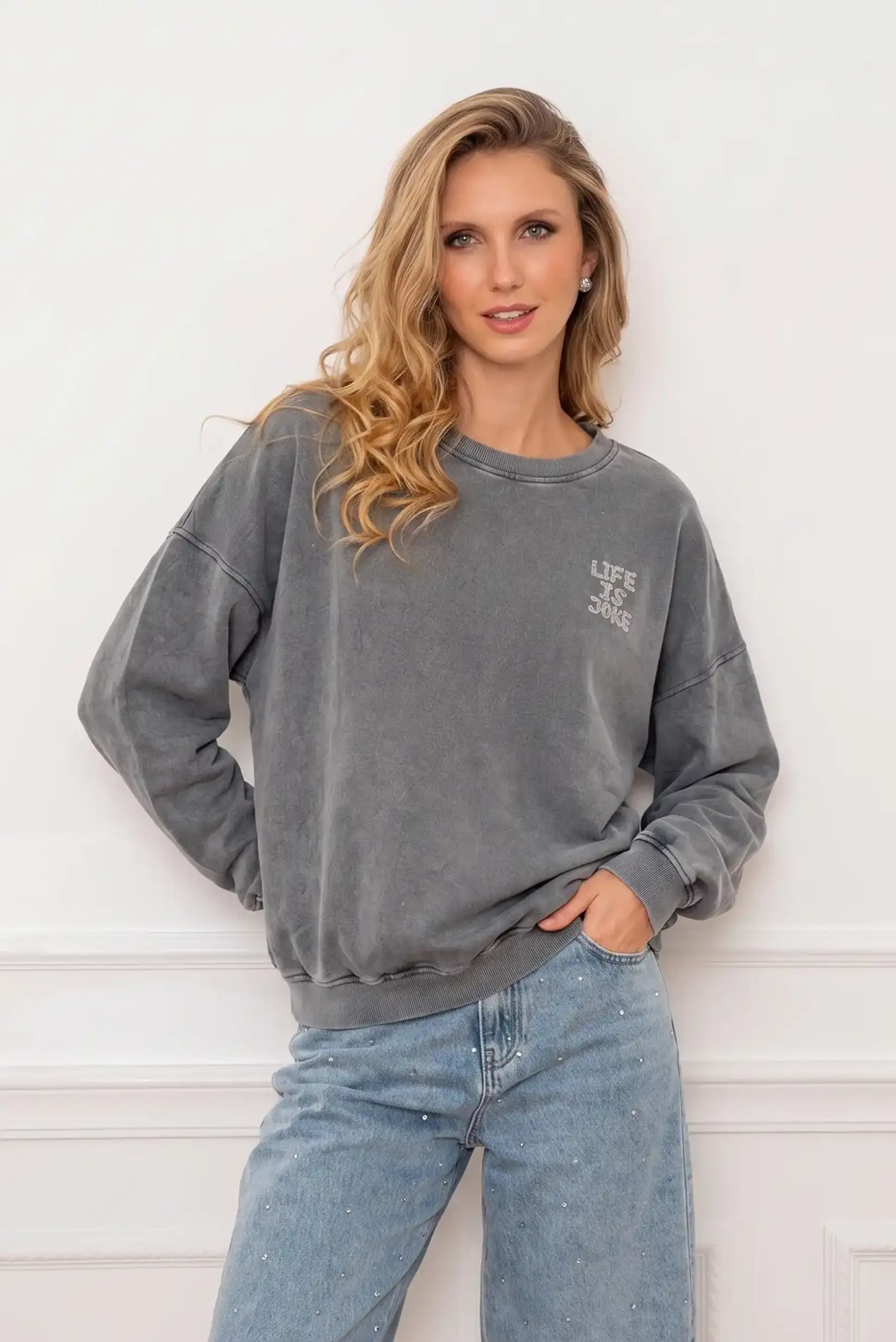 Mujer con sudadera gris lavada con texto y vaqueros claros con brillantes.