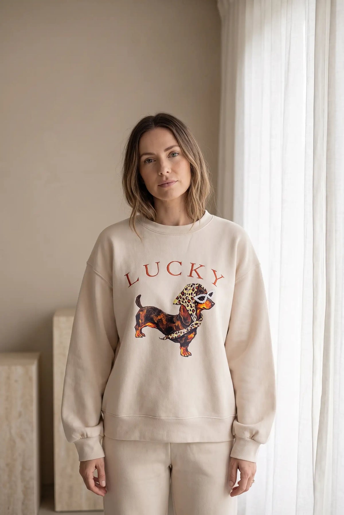 Mujer vistiendo sudadera beige de CHICA del Sur con estampado de perro Lucky y pedrería.