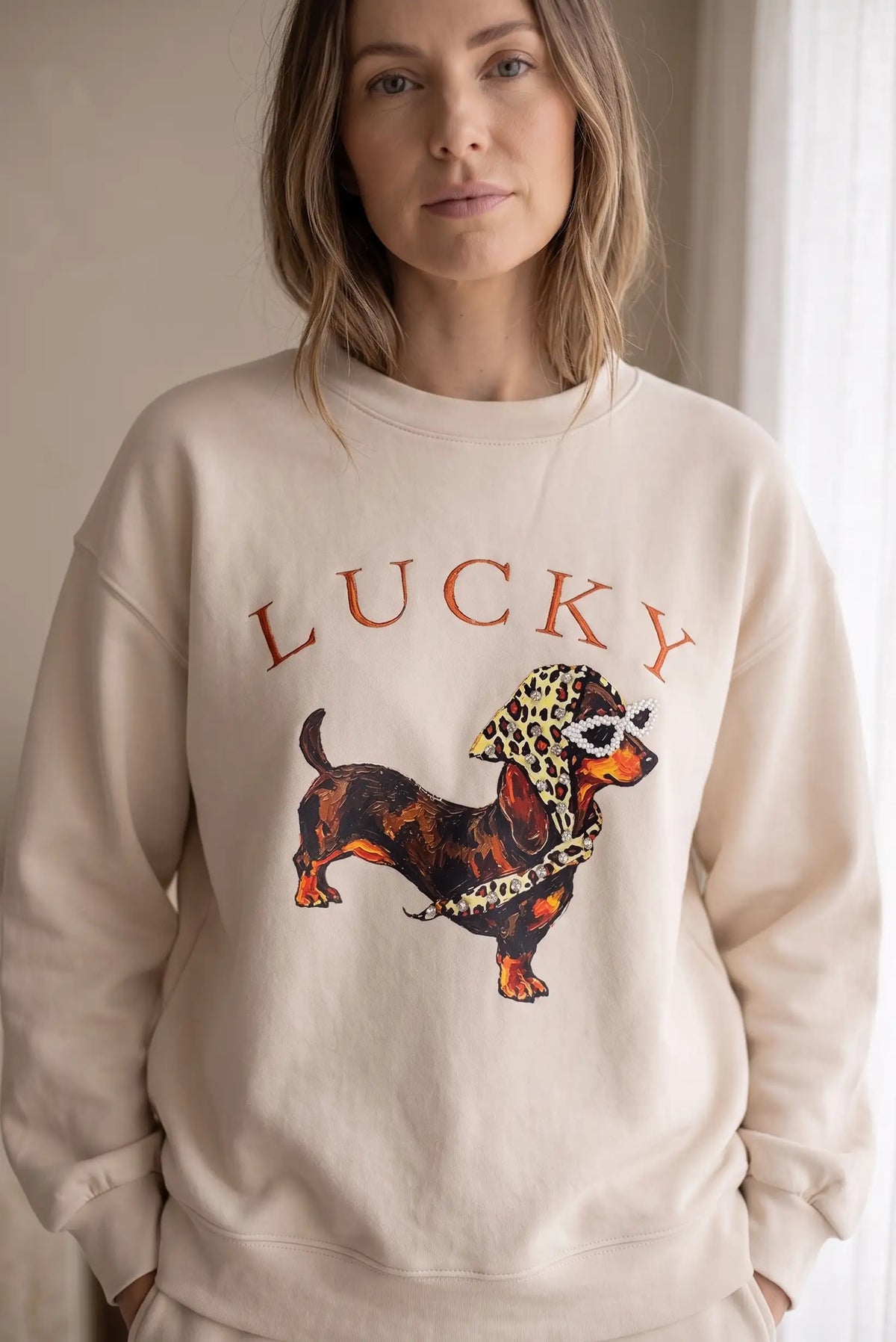 Mujer vistiendo sudadera beige de CHICA del Sur con estampado de perro Lucky y pedrería.