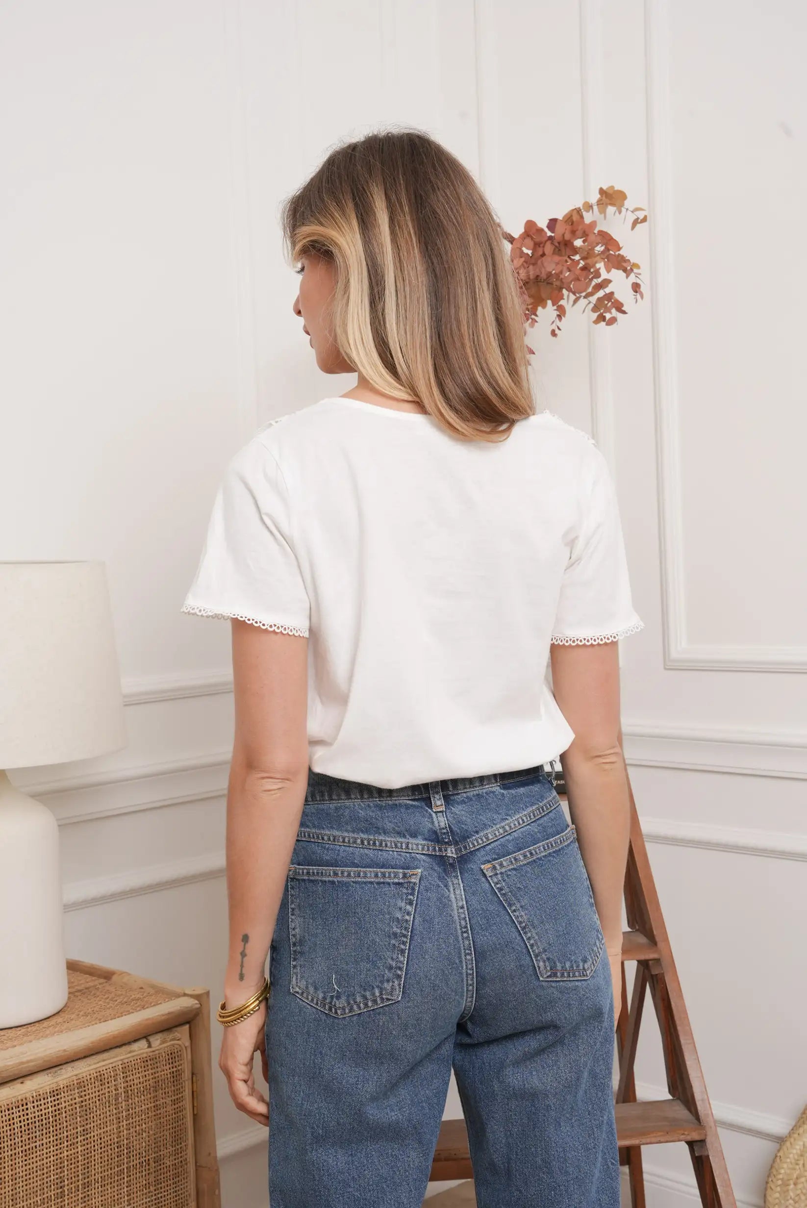Mujer de espaldas con top blanco de manga corta y jeans azul, estilo casual moderno.