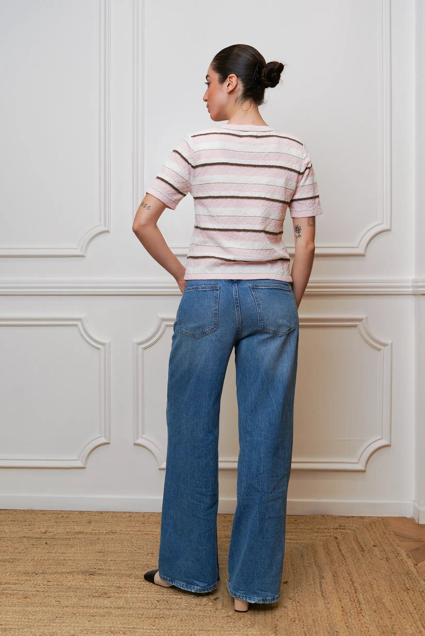 Mujer de espaldas con top de rayas rosa y pantalón vaquero ancho, estilo casual