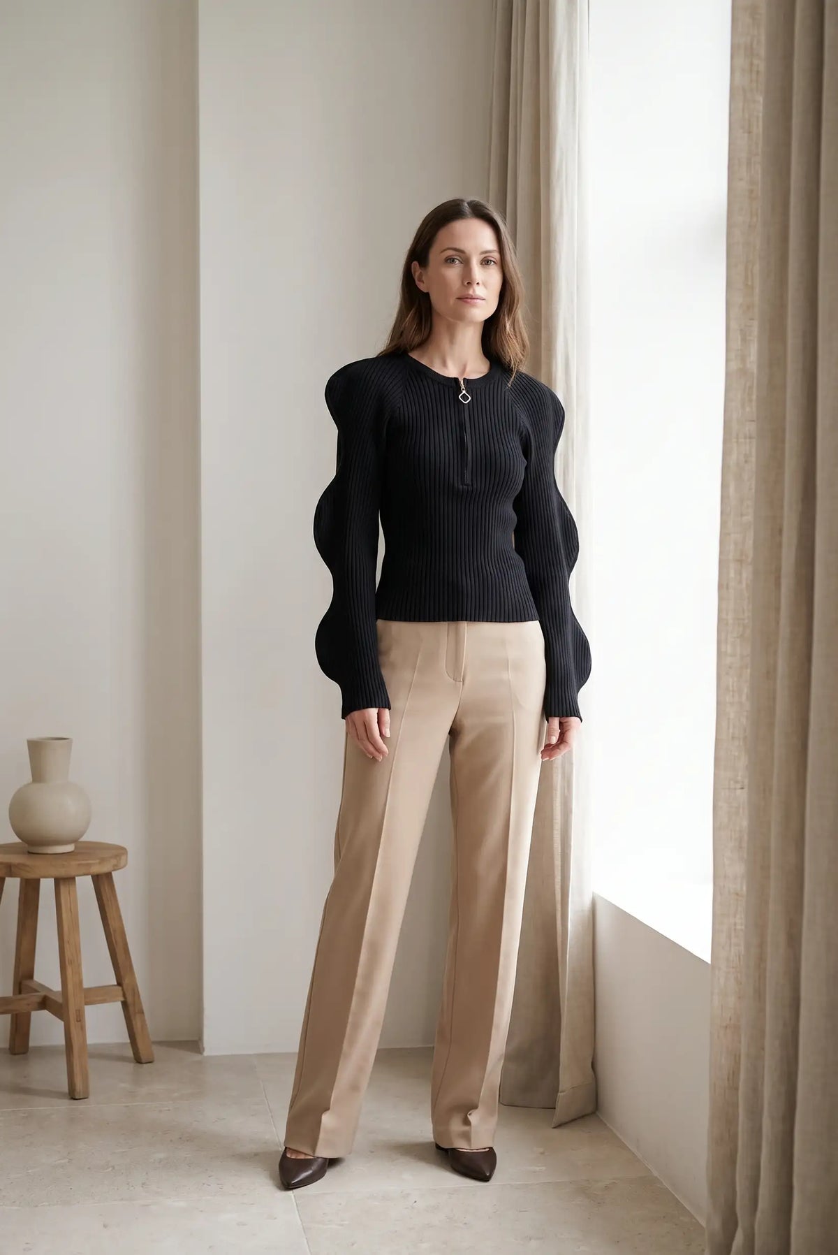 Mujer con top negro de punto canalé con mangas abullonadas y pantalones beige de CHICA del Sur