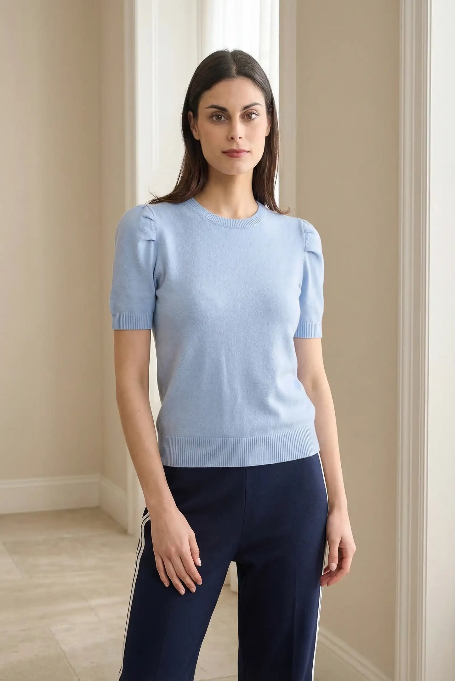 Mujer con top azul pastel de manga corta, estilo casual, en ambiente interior luminoso.