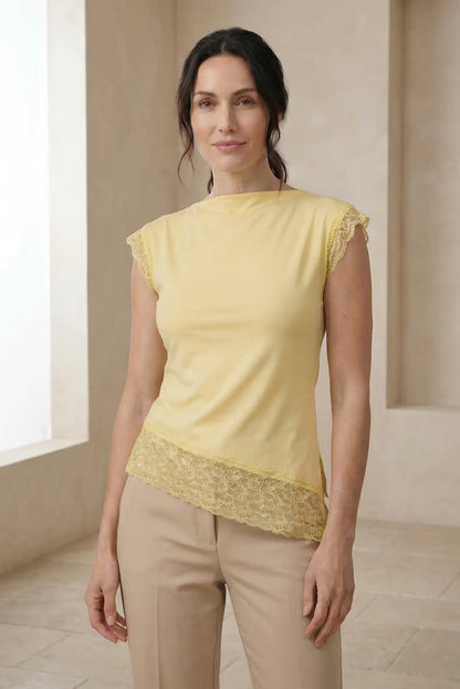 Mujer con top amarillo pastel de encaje, estilo casual primavera, pantalón beige, fondo neutro.