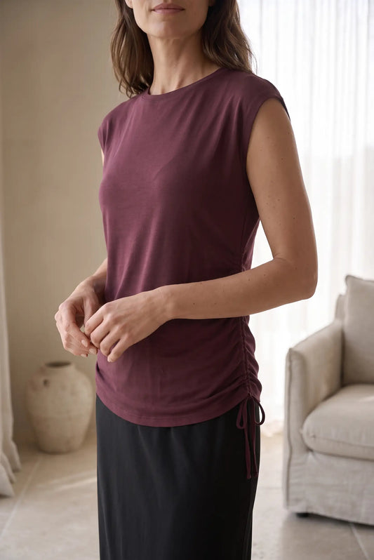 Mujer vistiendo camiseta sin mangas color burdeos con detalle de lazada lateral y falda negra.