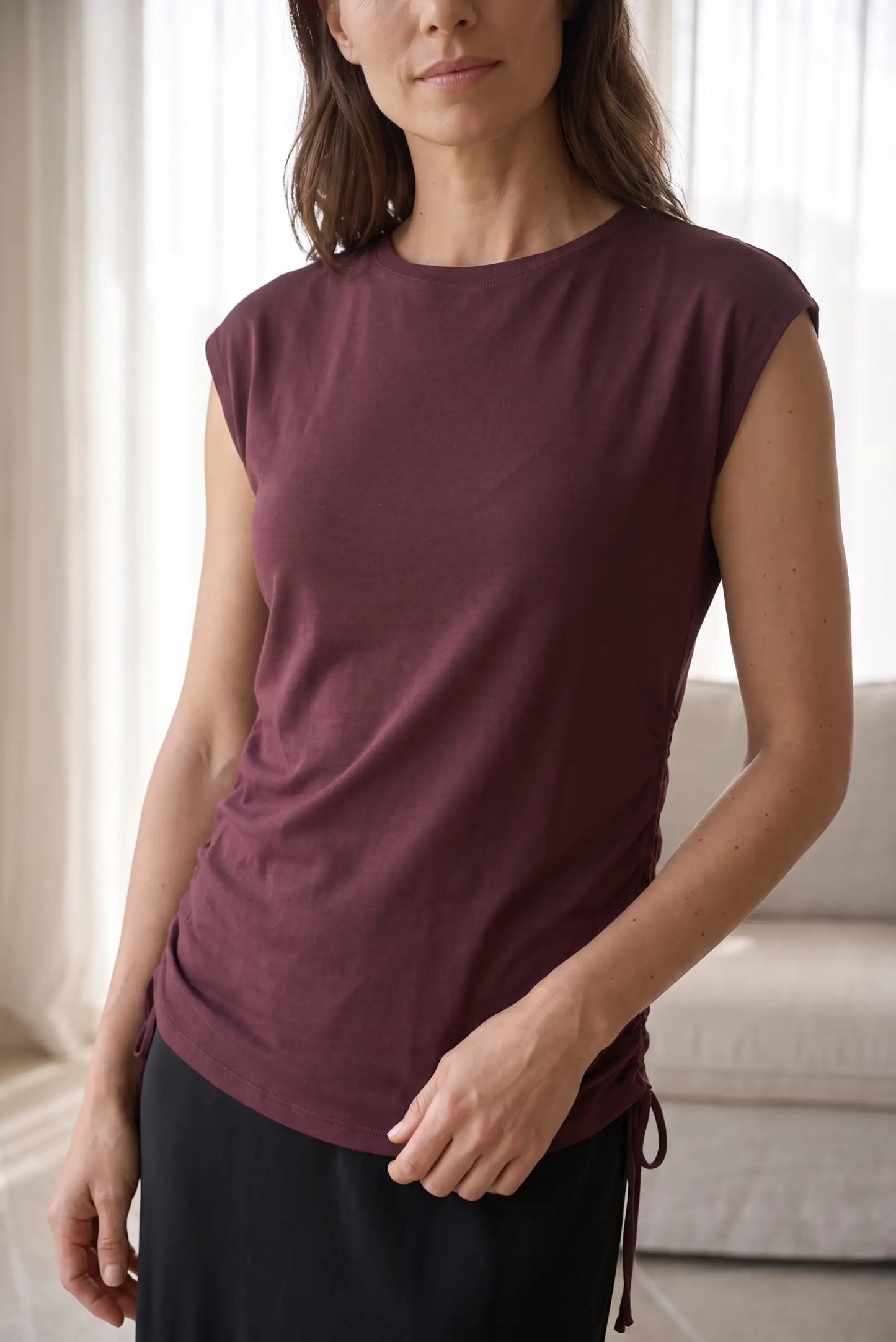 Mujer vistiendo camiseta sin mangas color burdeos con detalle de lazada lateral.