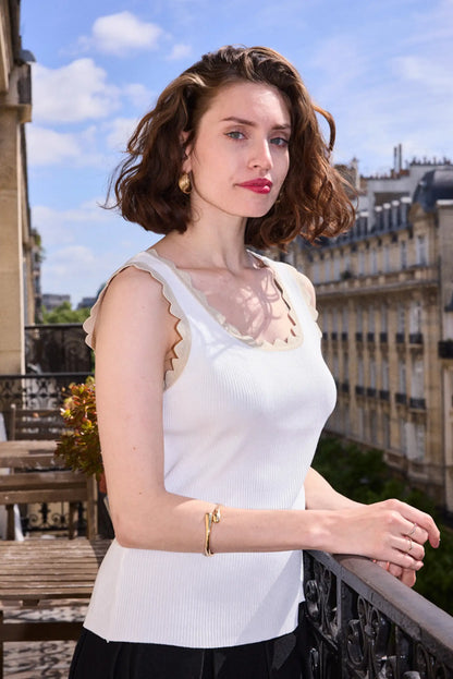 Mujer con top sin mangas blanco y detalles dorados, moda femenina de verano en balcón urbano