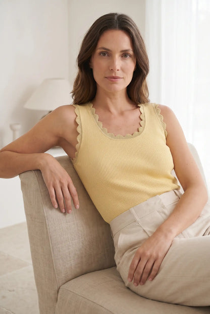 Mujer con top sin mangas amarillo de punto y detalles ondulados, sentada en sofá beige