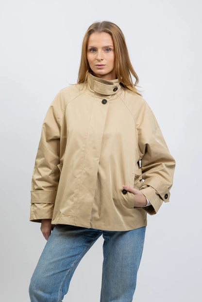 Mujer con cazadora trench beige de primavera, corte amplio, combinada con vaqueros azules.