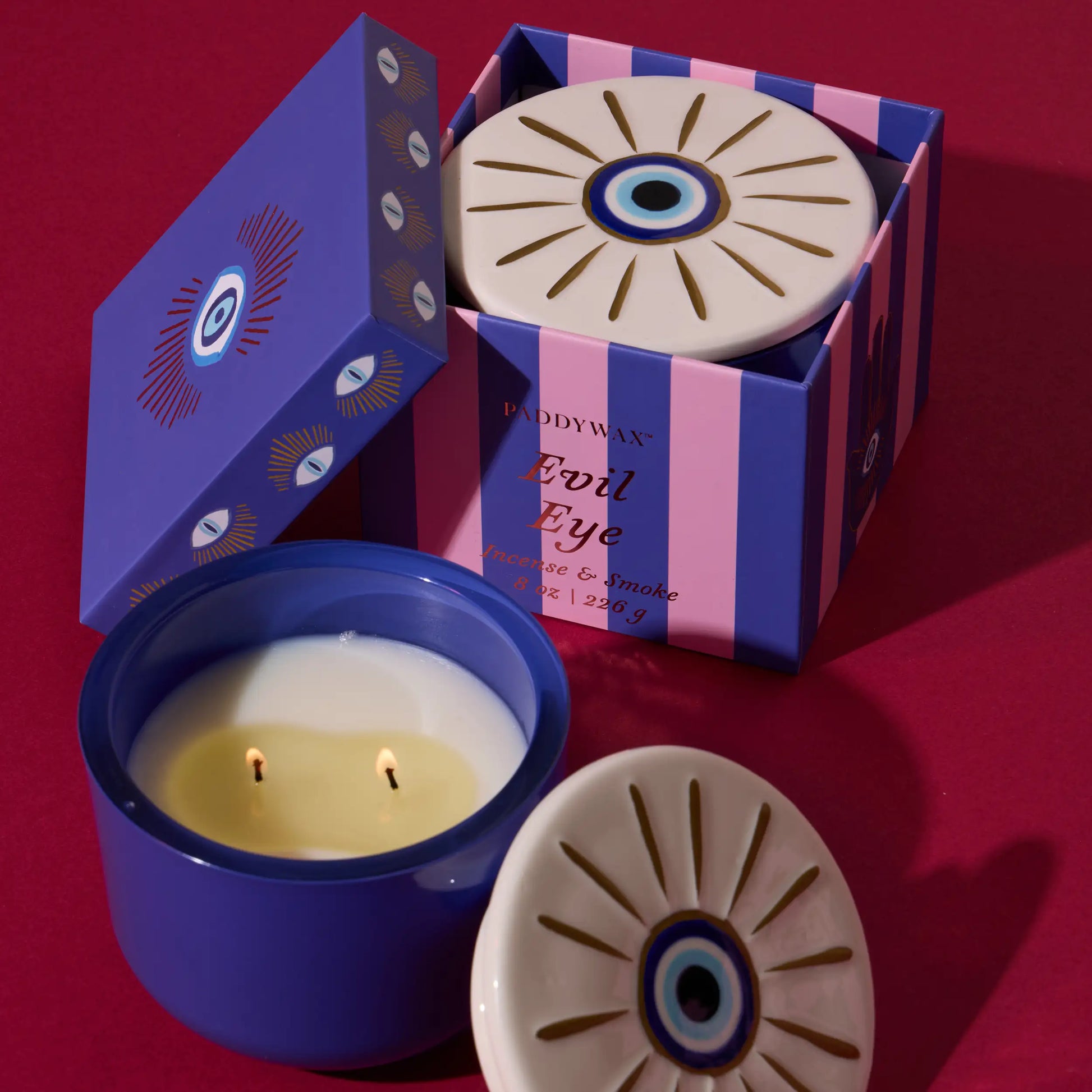Vela Paddywax Evil Eye en caja decorativa azul y rosa sobre fondo rojo, CHICA del Sur.