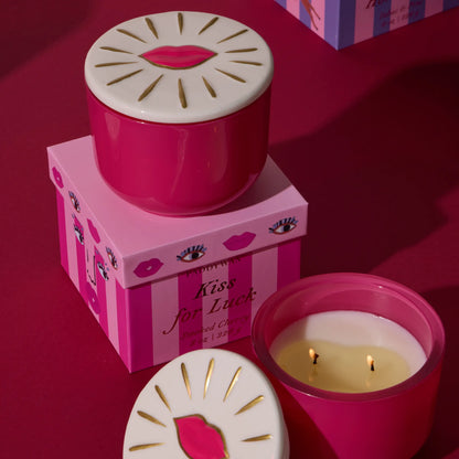 Vela aromática Paddywax Kiss for Luck, cereza ahumada, en envase rosa, sobre fondo rojo.