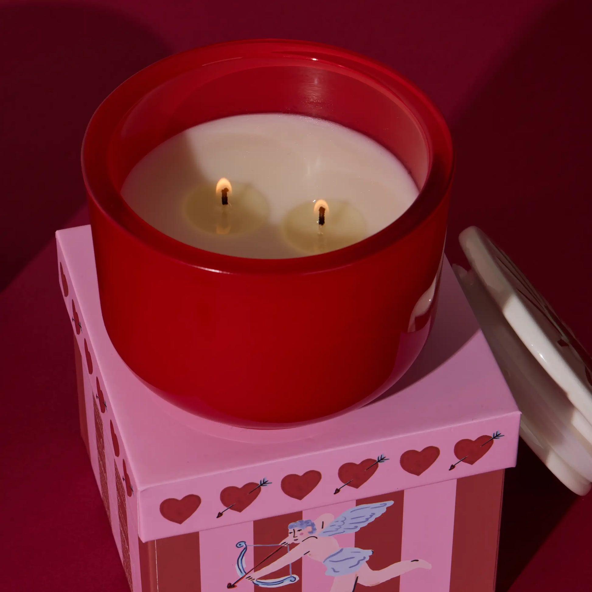Vela aromática roja con dos mechas sobre caja rosada decorada con corazones y cupido, CHICA del Sur
