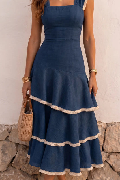 Vestido azul con volantes y borlas, ideal para verano, combinado con bolso de paja y accesorios dorados