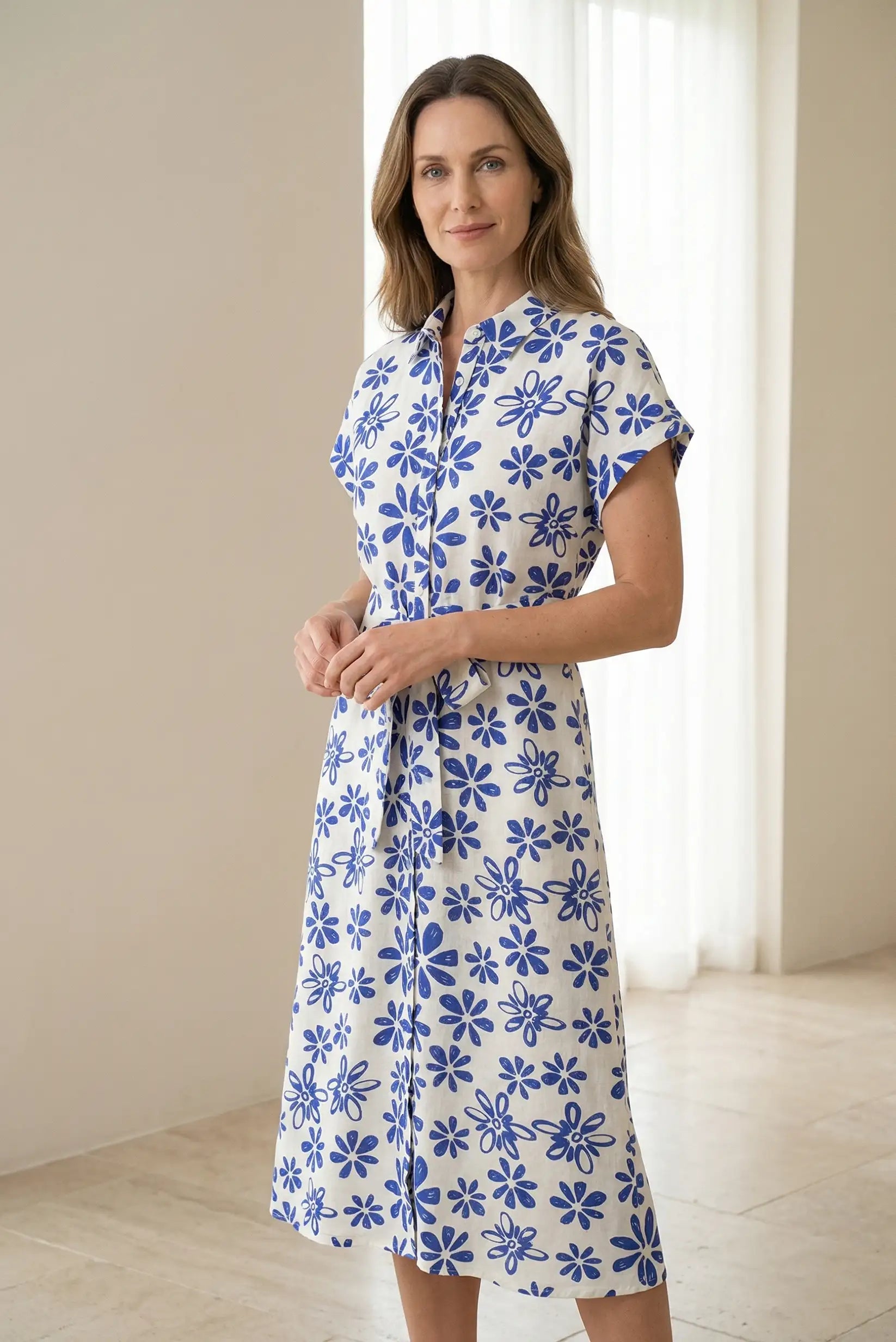Mujer con vestido largo blanco de manga corta y estampado floral azul en fondo interior luminoso