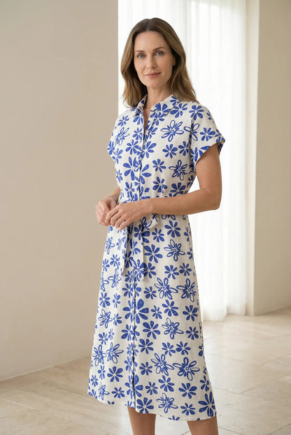 Mujer con vestido largo blanco de manga corta y estampado floral azul en fondo interior luminoso