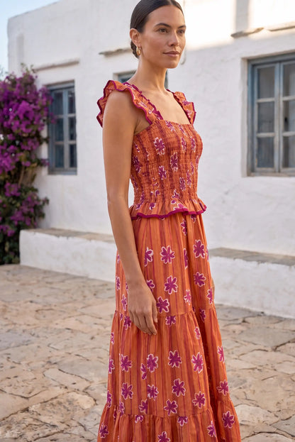 Vestido largo naranja con flores moradas, diseño con volantes y cintura elástica, ideal para verano.