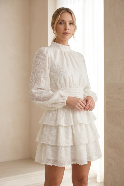 Mujer con vestido corto beige de manga larga y volantes, look veraniego elegante
