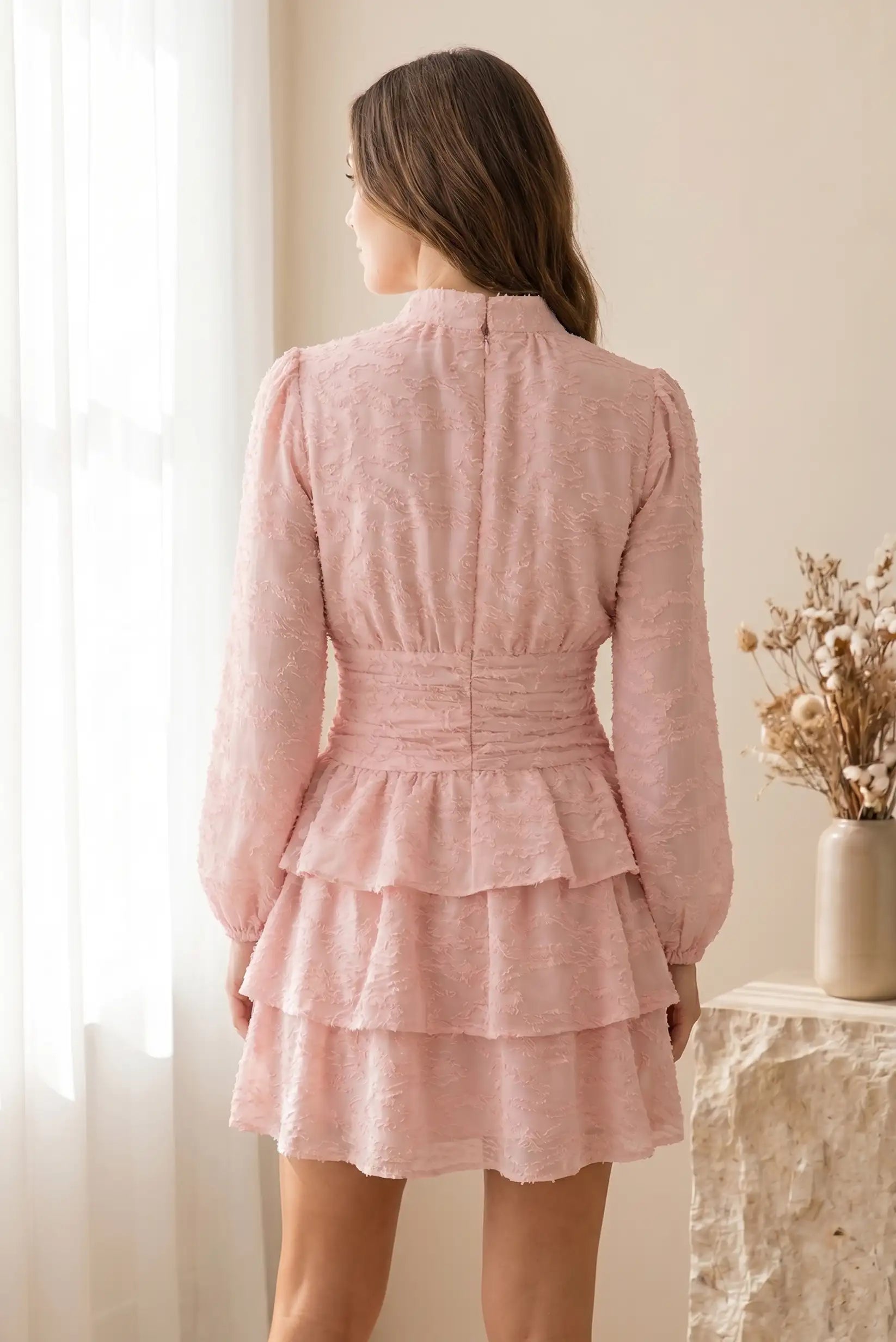 Mujer con vestido corto rosa de manga larga y volantes, estilo primavera, vista trasera