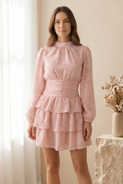 Mujer con vestido corto rosa de manga larga y tejido texturizado, en ambiente luminoso y primaveral.