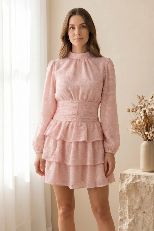 Mujer con vestido corto rosa de manga larga y tejido texturizado, en ambiente luminoso y primaveral.