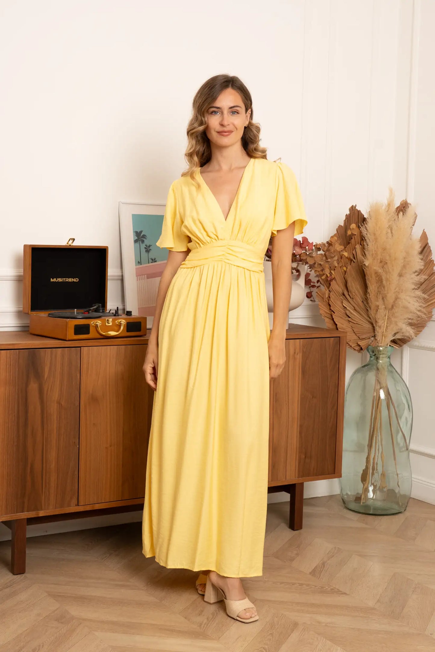 Mujer con vestido largo amarillo pastel, escote en V, en ambiente primaveral elegante