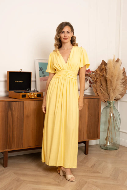 Mujer con vestido largo amarillo pastel, escote en V, en ambiente primaveral elegante
