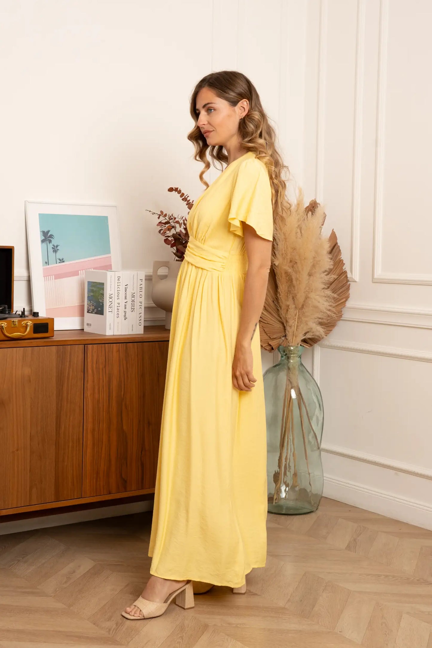 Mujer con vestido largo amarillo pastel de primavera en interior elegante, moda femenina casual