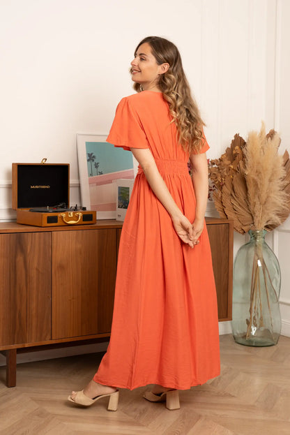 Mujer con vestido largo terracota, sandalias de tacón, en ambiente moderno y decorativo.