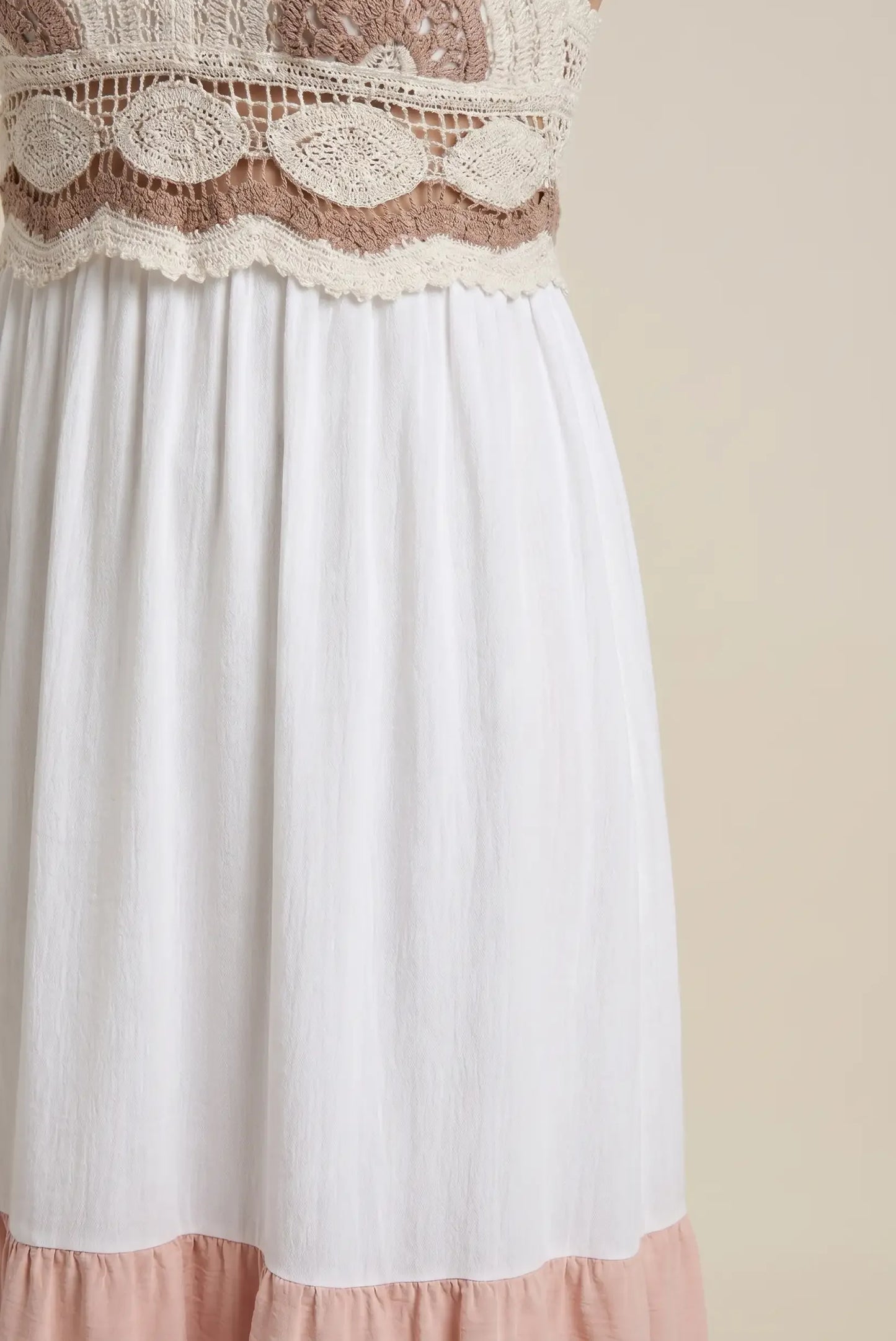 Detalle de vestido largo de mujer, blanco con cuerpo de crochet beige y falda con volante rosa.