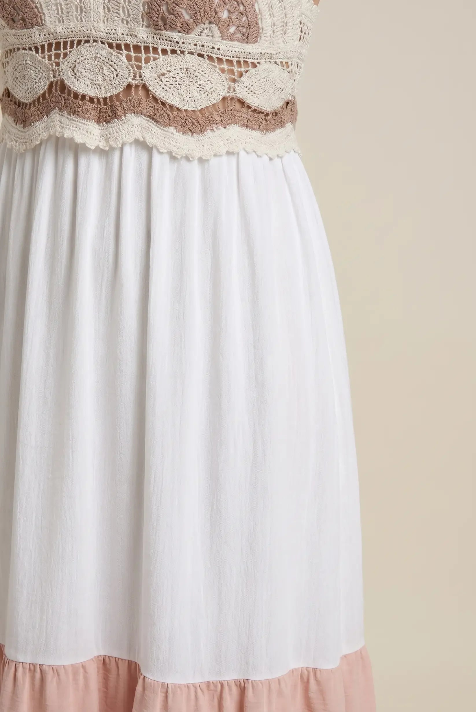 Detalle de vestido largo de mujer, blanco con cuerpo de crochet beige y falda con volante rosa.